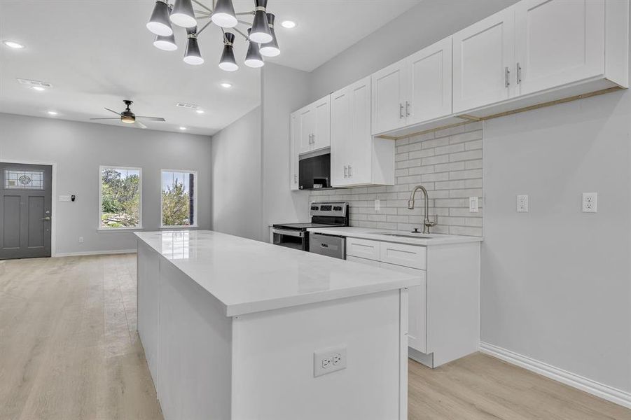Kitchen featuring appliances with stainless steel finishes, light hardwood / wood-style flooring, white cabinets, sink, and a kitchen island