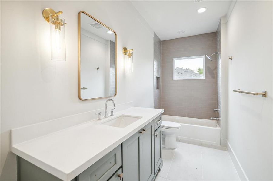 Oversized tile adds interest in this guest bathroom while remaining timeless and neutral. Quartz countertops are set atop a sage green vanity, contrasting nicely with the milky white walls.