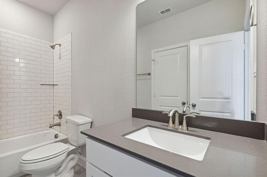 Full bathroom featuring tiled shower / bath combo, vanity, and toilet