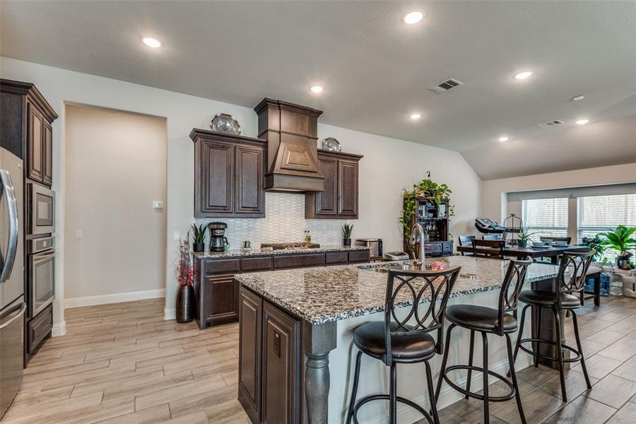 Kitchen featuring light stone countertops, lofted ceiling, appliances with stainless steel finishes, and a kitchen island with sink