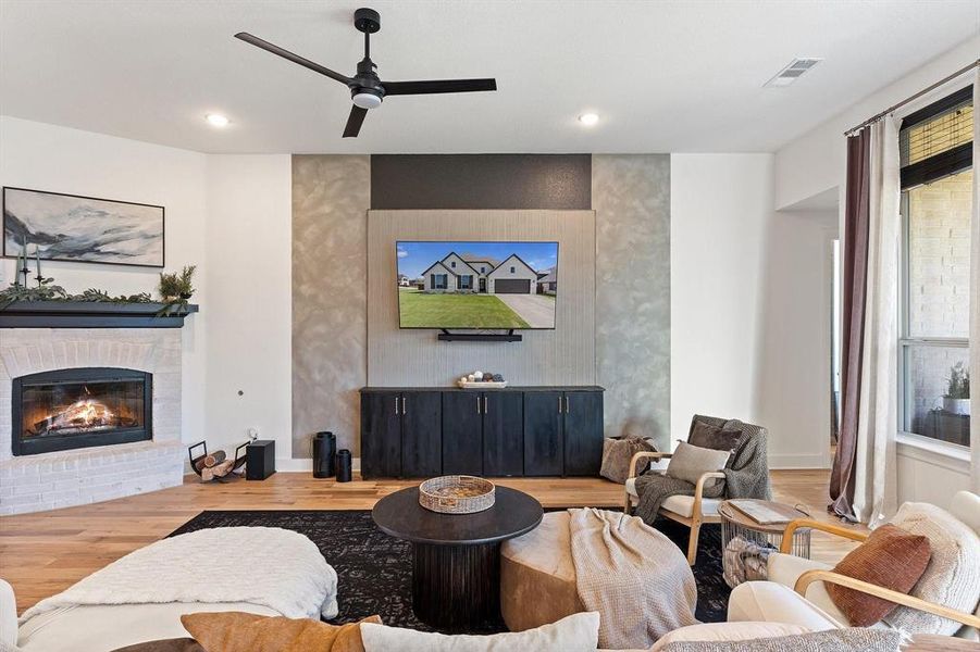 Living room featuring ceiling fan, wood-type flooring, and a brick fireplace