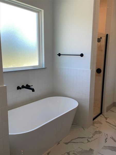 Bathroom featuring tile flooring, separate shower and tub, and tile walls