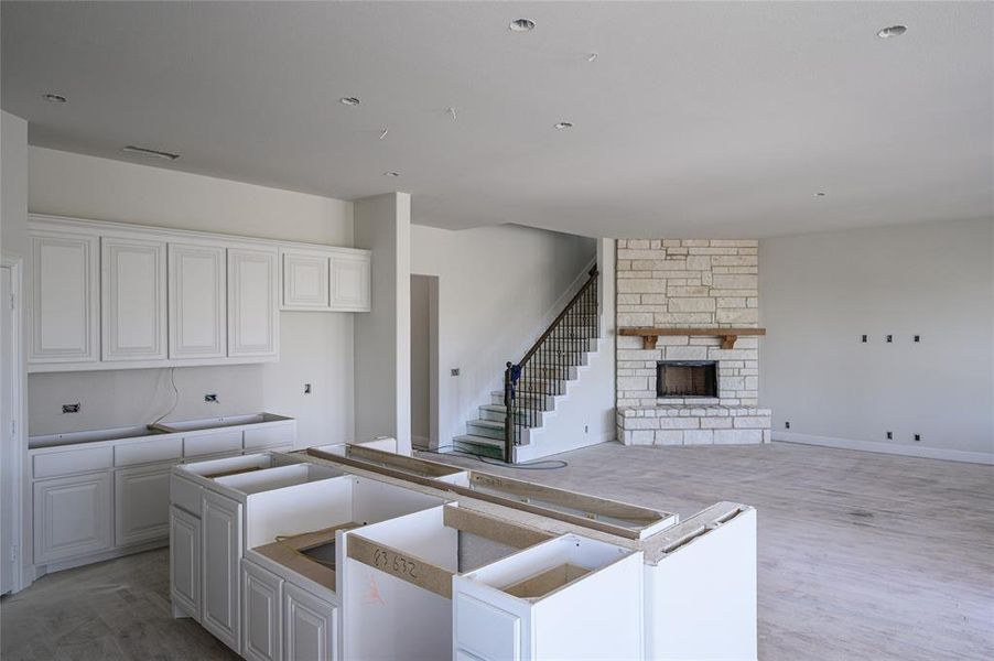 Kitchen featuring white cabinets, a stone fireplace, a center island, and light wood-type flooring