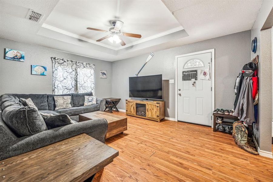 Living room featuring hardwood / wood-style floors, ceiling fan, a raised ceiling, and ornamental molding