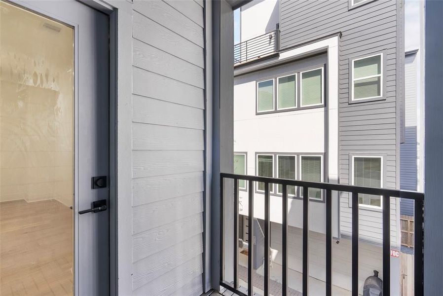 This is a view from a balcony with a metal railing, showing a glimpse into a modern residential area with multi-story homes featuring a neutral color palette and contemporary design.