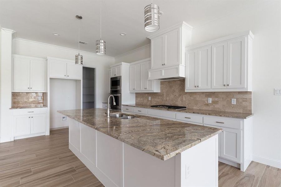 Kitchen with stainless steel appliances, crown molding, an island with sink, white cabinets, and backsplash