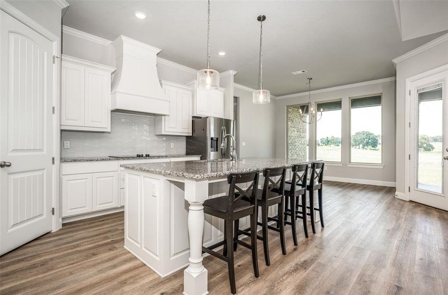 Kitchen with wood-type flooring, tasteful backsplash, white cabinets, a center island with sink, and custom range hood