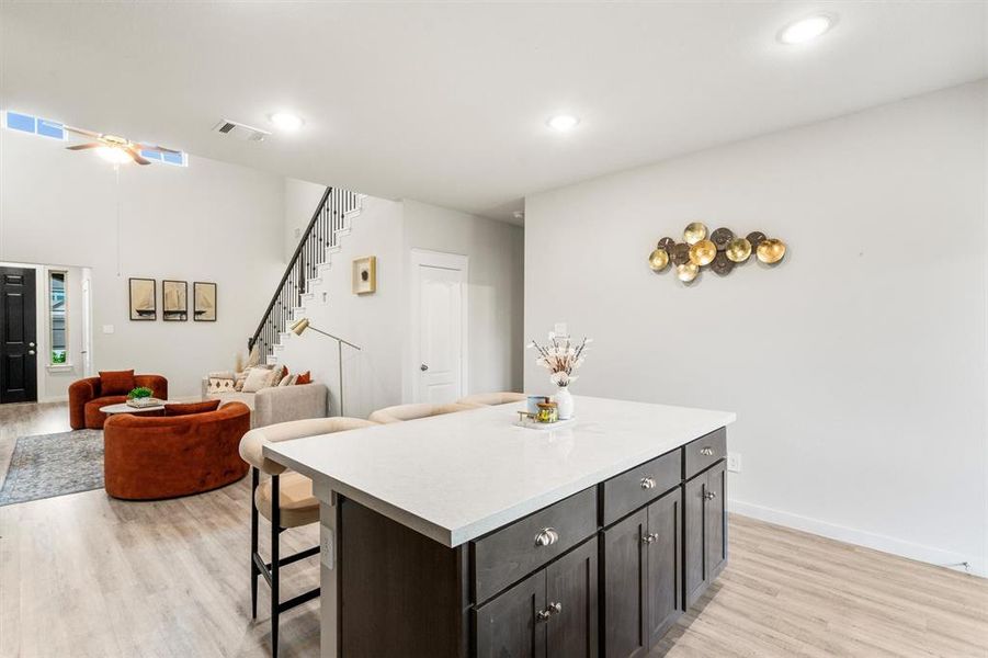 Kitchen featuring a kitchen island, light hardwood / wood-style floors, ceiling fan, dark brown cabinetry, and a breakfast bar