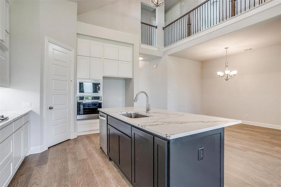 Kitchen with light stone counters, sink, white cabinetry, hanging light fixtures, and appliances with stainless steel finishes