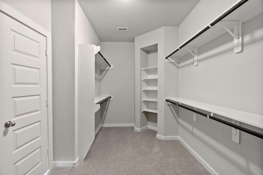 Experience luxury in this spacious walk-in closet with high ceilings and plush carpet. Warm paint tones, built-in shelving, and dark finishes create a contemporary and functional retreat Sample photo of completed home. As-built color and selections may vary.
