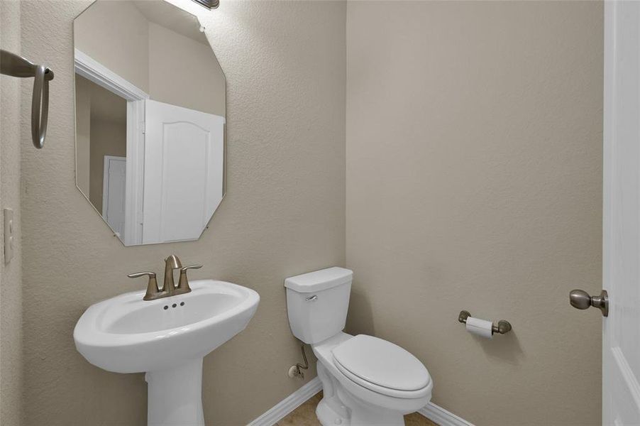 Half bathroom features a pedestal sink, toilet, and an octagonal mirror above the sink.