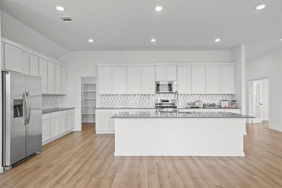 Spacious gourmet kitchen with Walk-in Pantry, with white cabinetry, stainless steel appliances, quartz countertop, Breakfast bar, with wood flooring. It features beautiful backsplash tile with gas stove and recessed lighting