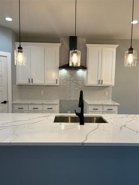 Kitchen with hanging light fixtures, light stone countertops, range hood, and tasteful backsplash