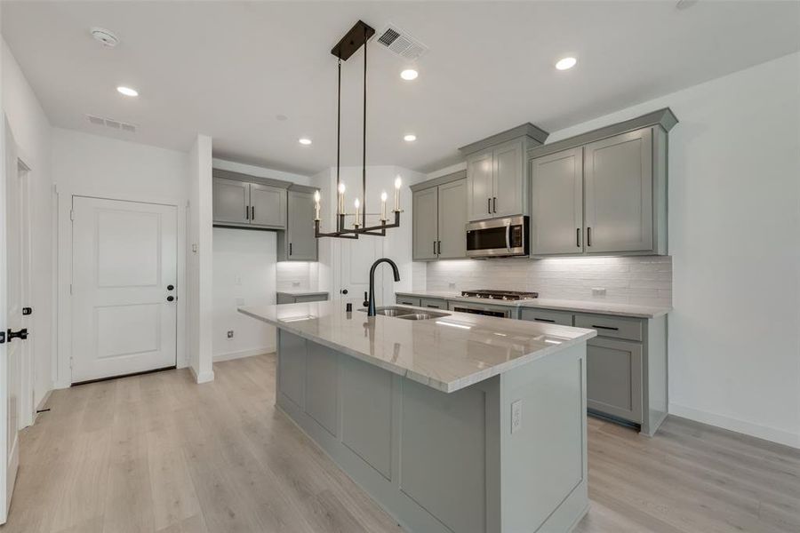 Kitchen featuring sink, light stone counters, hanging light fixtures, a kitchen island with sink, and light wood-type flooring