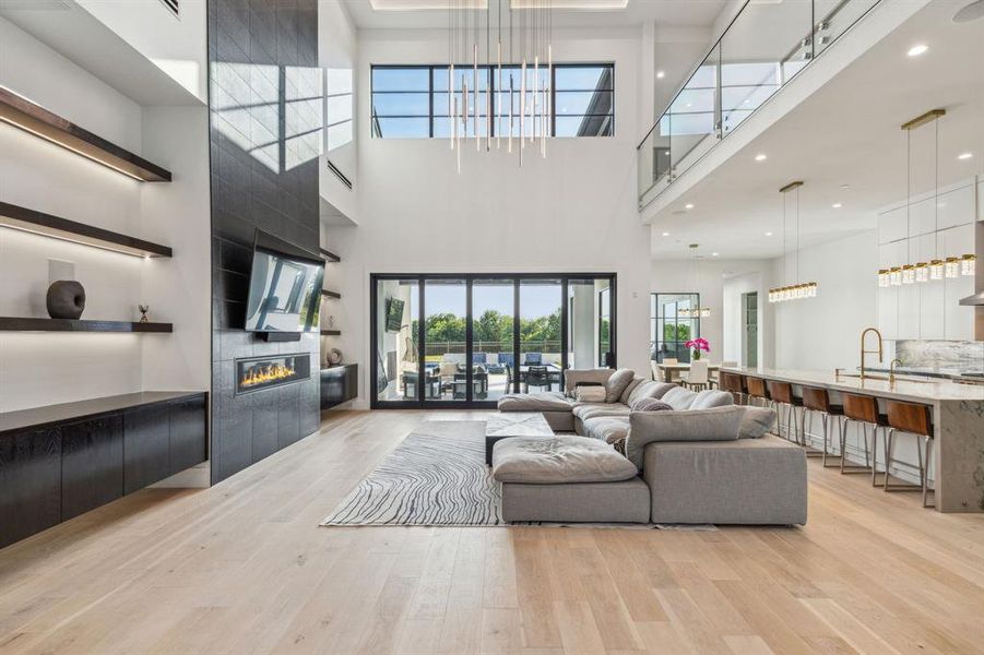 Living room featuring a fireplace, an inviting chandelier, light wood-type flooring, and a high ceiling