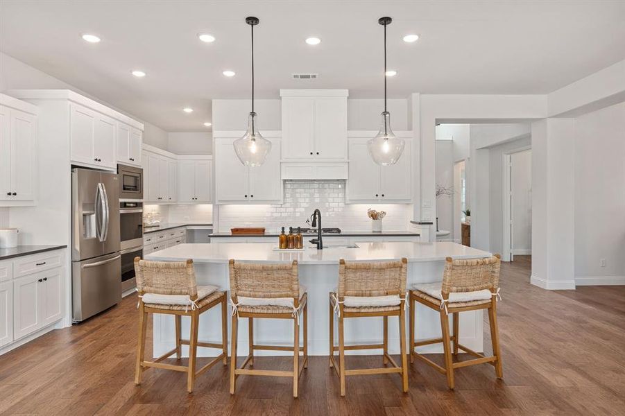 Kitchen with tasteful backsplash, a kitchen bar, appliances with stainless steel finishes, hardwood / wood-style flooring, and a center island with sink