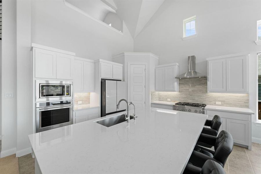 Kitchen with stainless steel appliances, light tile floors, wall chimney range hood, high vaulted ceiling, and sink
