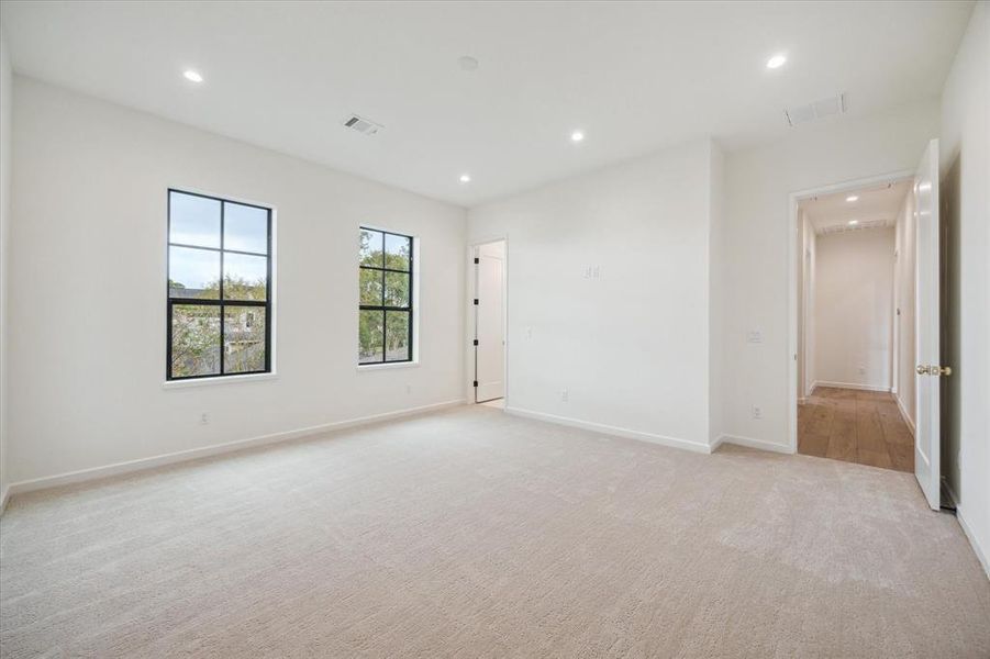 Carpeted bedroom with ample space and two large windows allowing natural light to flood the room. The neutral color palette creates a clean and inviting atmosphere.