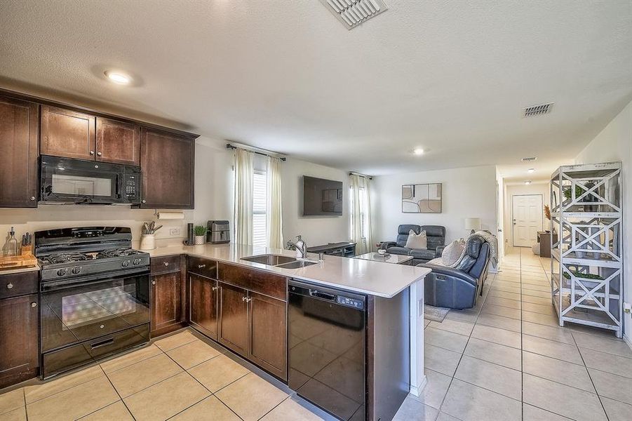 Kitchen featuring kitchen peninsula, sink, black appliances, and dark brown cabinets