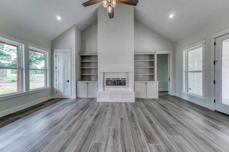 Unfurnished living room with high vaulted ceiling, light wood-type flooring, and ceiling fan