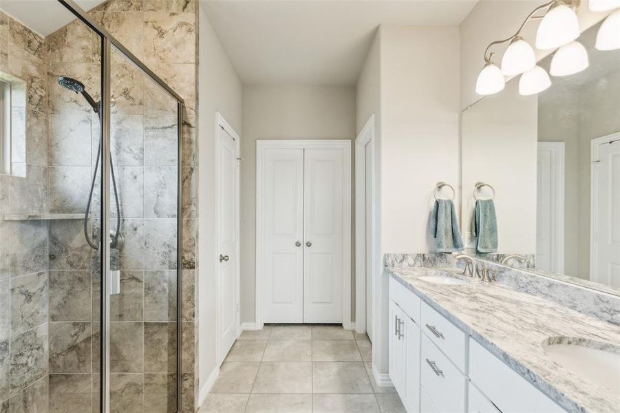 Bathroom featuring vanity with extensive cabinet space, an enclosed shower, dual sinks, and tile floors