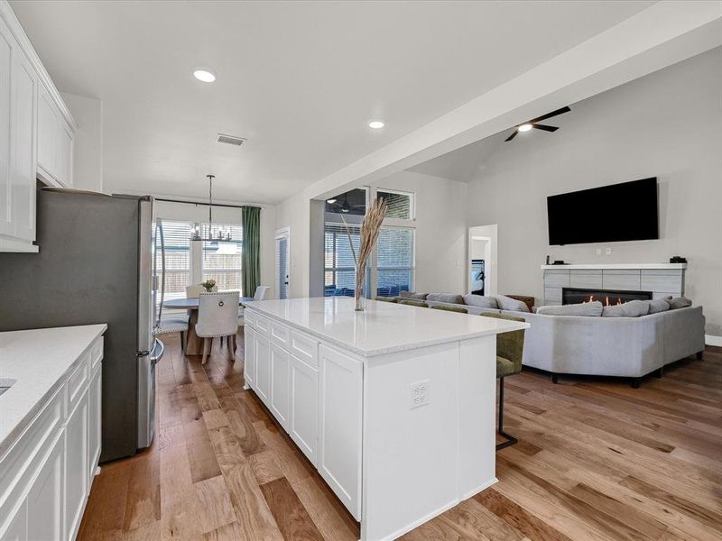 Kitchen featuring an island with sink, white cabinetry, stainless steel refrigerator, light hardwood / wood-style floors, and decorative light fixtures