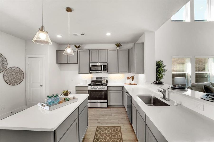 Kitchen with stainless steel appliances, gray cabinetry, sink, and a wealth of natural light