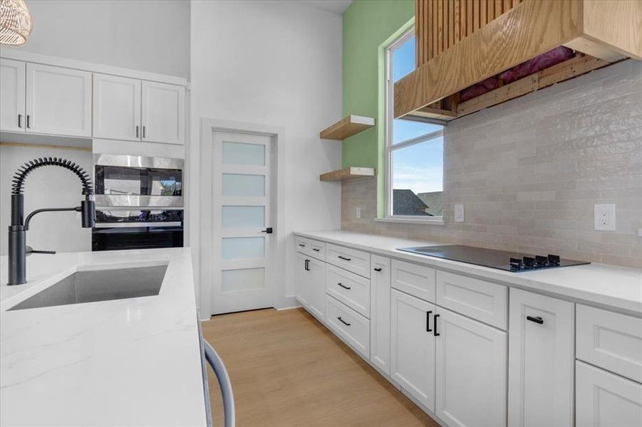 Kitchen with black electric cooktop, white cabinetry, sink, and light wood-type flooring