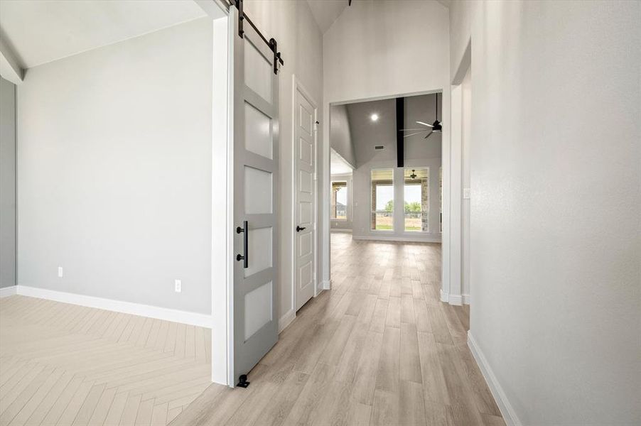 Hallway featuring light hardwood / wood-style flooring, a barn door, and a high ceiling