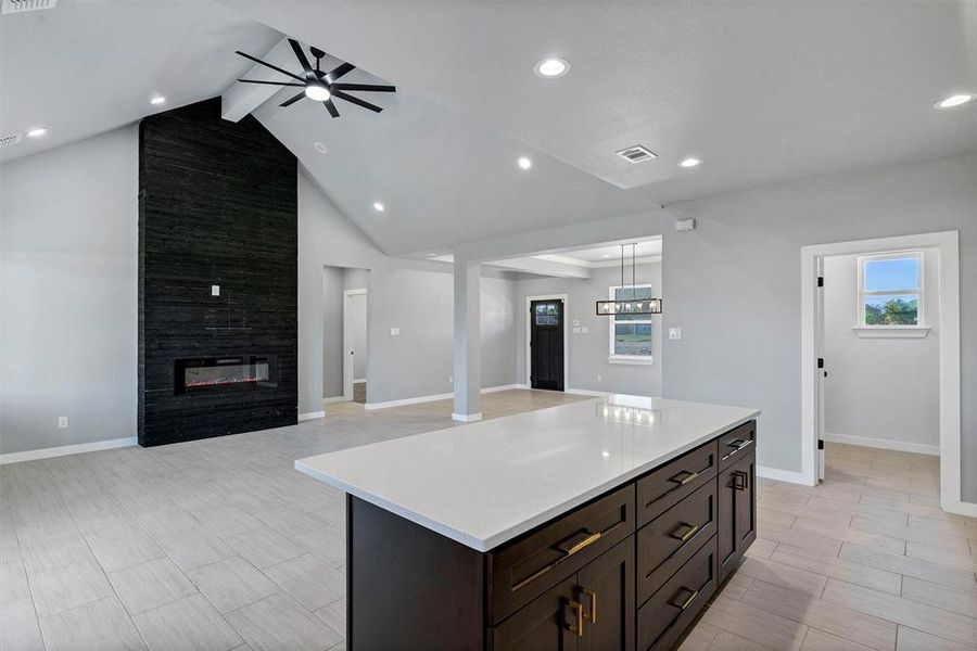 Kitchen featuring a fireplace, lofted ceiling with beams, a center island, ceiling fan with notable chandelier, and light hardwood / wood-style floors