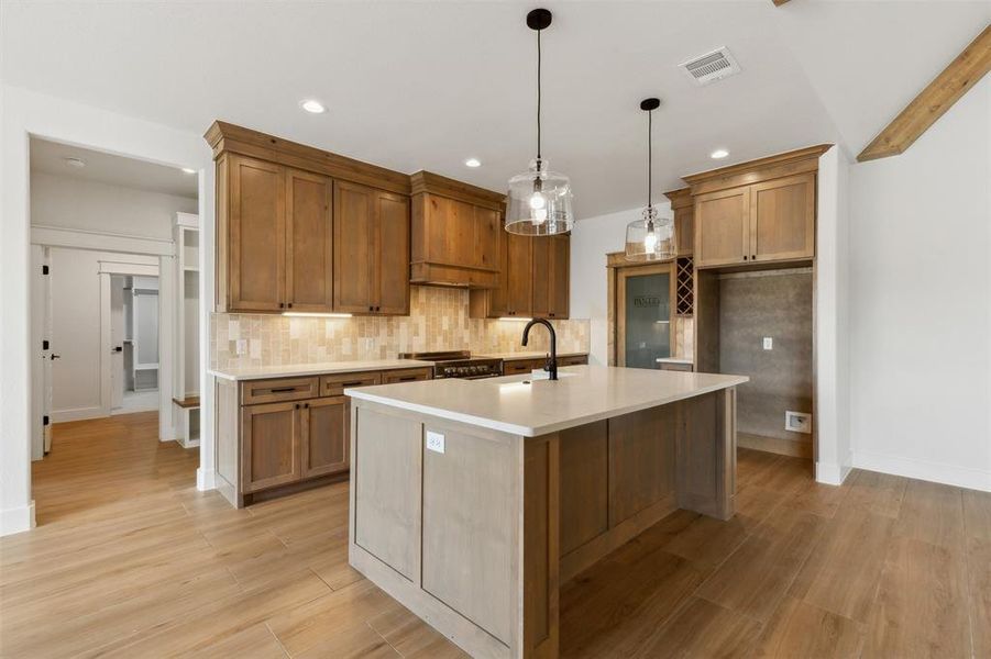 Kitchen with tasteful backsplash, decorative light fixtures, an island with sink, sink, and light hardwood / wood-style floors