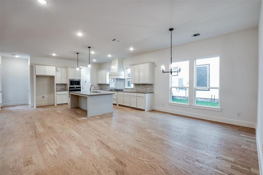 Kitchen with a kitchen island with sink, light hardwood / wood-style flooring, sink, custom range hood, and decorative light fixtures