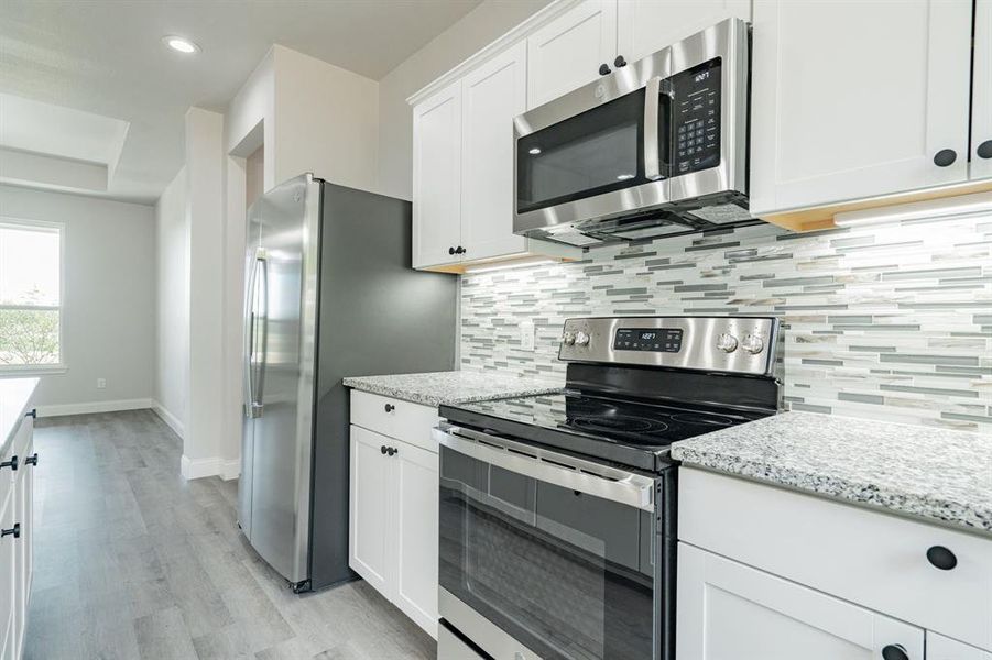 Kitchen with appliances with stainless steel finishes, decorative backsplash, light wood-type flooring, light stone countertops, and white cabinetry