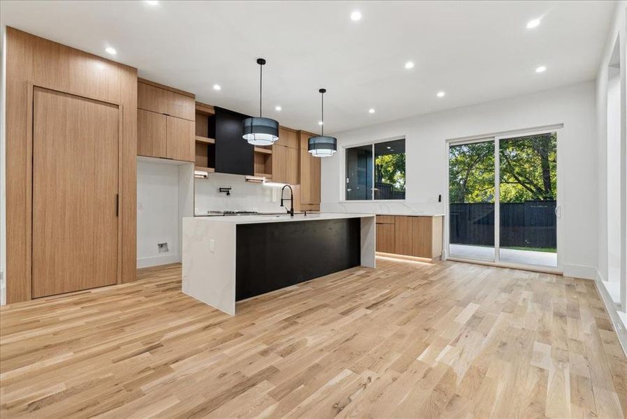 Kitchen with pendant lighting, light hardwood / wood-style floors, a center island with sink, and backsplash