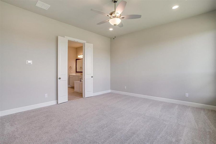 Unfurnished bedroom featuring ensuite bath, light carpet, and ceiling fan