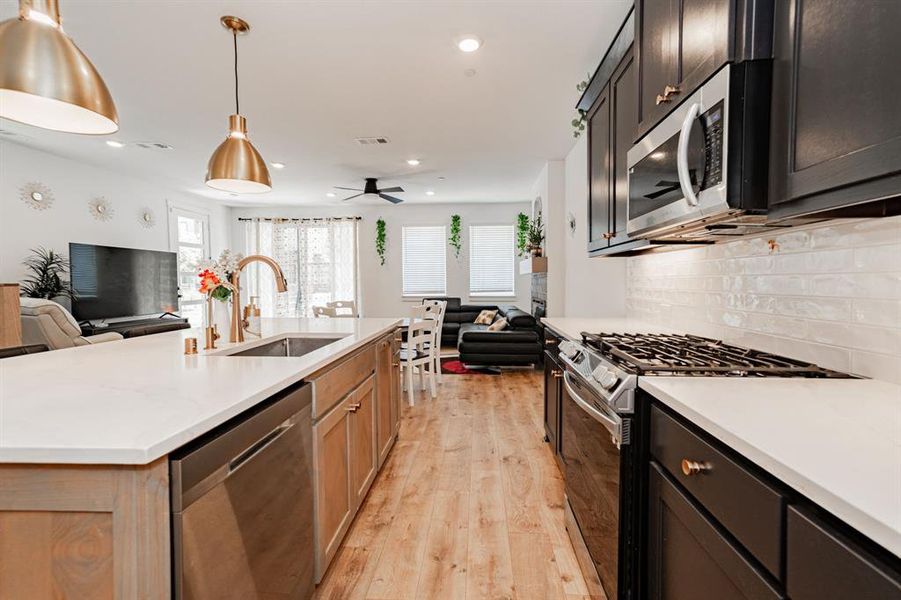 Kitchen with appliances with stainless steel finishes, light hardwood / wood-style flooring, decorative backsplash, a kitchen island with sink, and ceiling fan