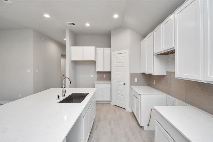 Culinary haven, featuring a massive island, granite countertops, a tile backsplash, stainless steel appliances (to be installed), and 42” upper cabinets. Sample photo of similar plan. As-built color and selections may vary.