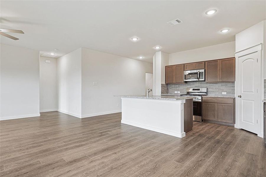 Kitchen with appliances with stainless steel finishes, dark wood-type flooring, light stone counters, decorative backsplash, and a kitchen island with sink