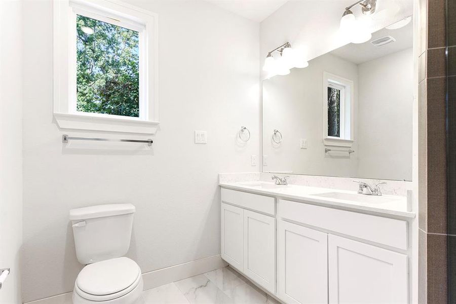 Picture of the primary bathroom with his/her sinks, quartz countertops, white cabinets, large white tile floors, and a window.