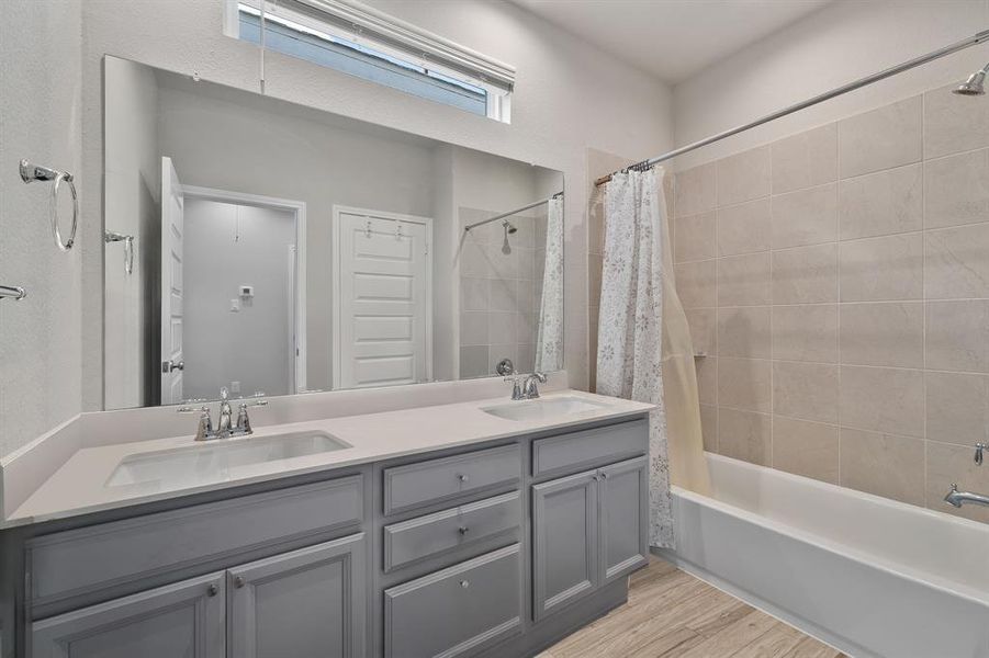 Secondary bathroom features light countertops and grey cabinets, neutral paint, shower/tub combo with tile surround, large mirror, tile floors, sleek fixtures and modern finishes, plenty of space to accommodate any visiting family or guests.