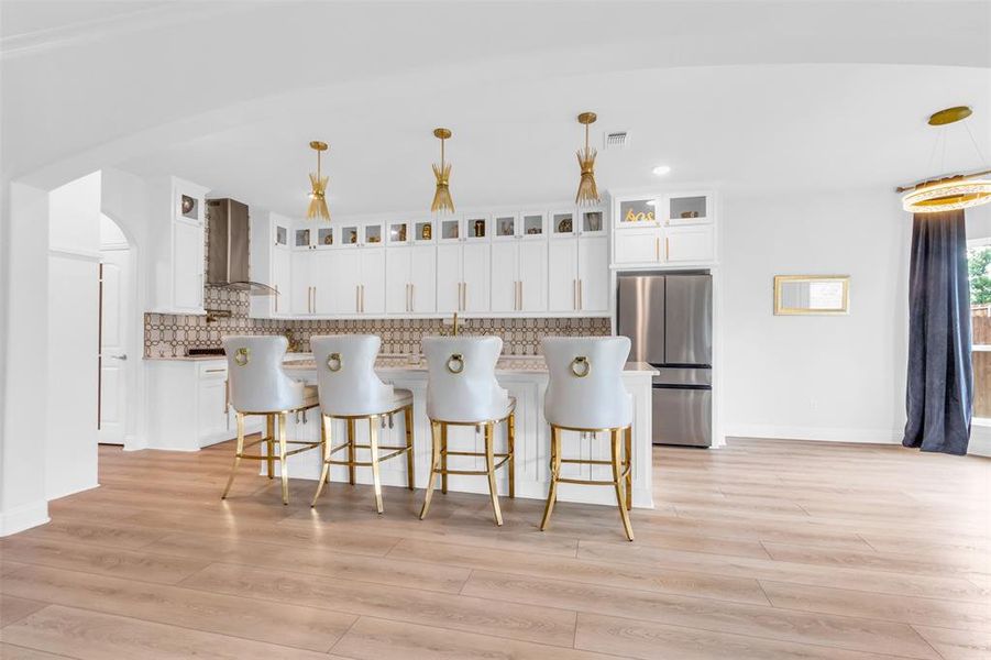 Kitchen featuring wall chimney range hood, stainless steel refrigerator, decorative light fixtures, decorative backsplash, and white cabinetry