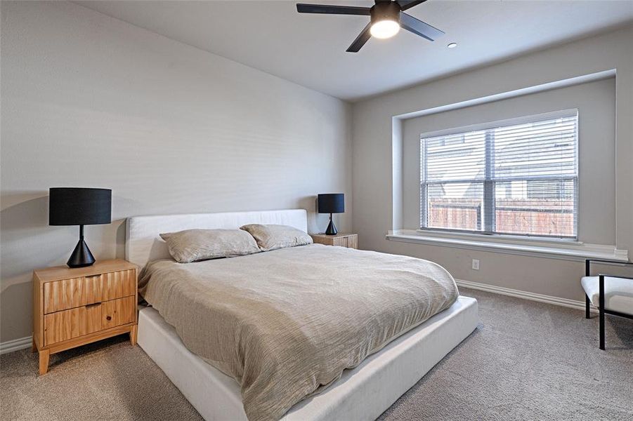 Spacious, carpeted primary bedroom with ceiling fan and bay window