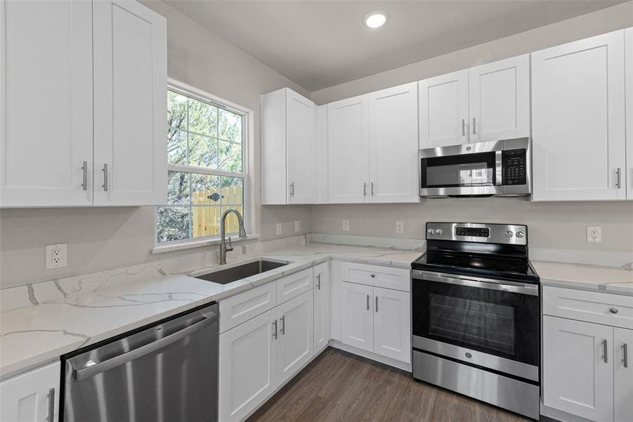 Kitchen with dark wood-type flooring, white cabinets, sink, and stainless steel appliances