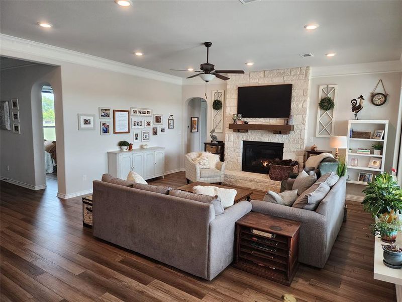 Living room with ornamental molding, ceiling fan, dark wood-type flooring, and a stone fireplace