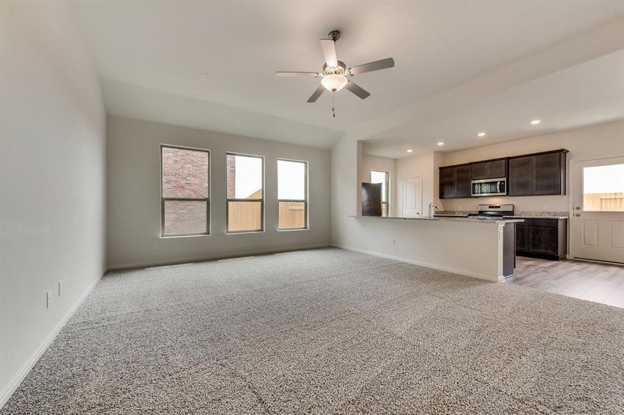 Unfurnished living room featuring ceiling fan, a wealth of natural light, and light colored carpet
