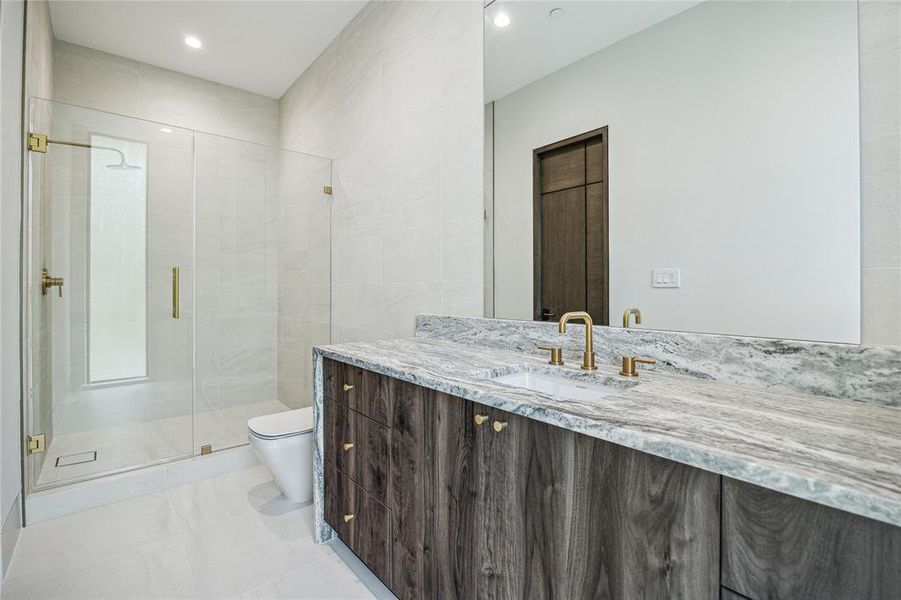 This luxurious guest bathroom is adorned with Passenger White floor and wall tiles that exude timeless elegance. Featuring Florida Leathered Quartzite countertops and a walk-in shower with a seamless glass door, this space offers both sophistication and functionality, complemented by designer neutral wall paint for a tranquil ambiance.