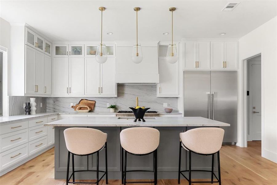 Kitchen featuring light wood-type flooring, a center island, light stone counters, and tasteful backsplash