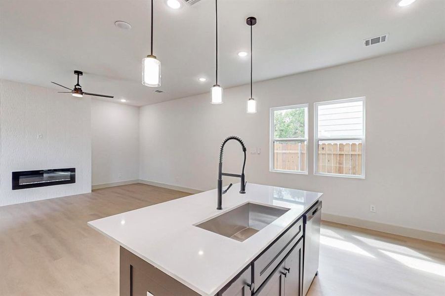 Kitchen featuring an island with sink, sink, light hardwood / wood-style floors, pendant lighting, and dishwasher