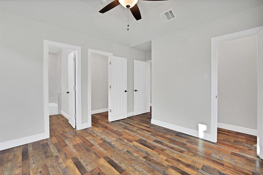 Unfurnished bedroom featuring a walk in closet, ensuite bathroom, dark wood-type flooring, and ceiling fan