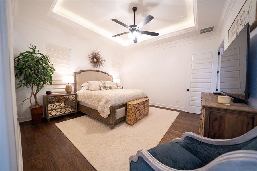 Bedroom featuring ceiling fan, ornamental molding, a tray ceiling, and dark hardwood / wood-style flooring